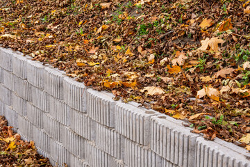 A retaining wall made of concrete elements protects the roadway and pavement from sliding down the slope. Autumn.