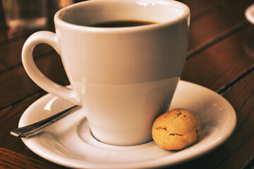 a cup of coffee served with a cookie on wooden table. Vintage, romantic coffee concept
