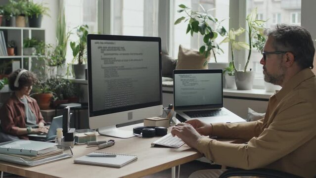 Mature professional programmer working with codes on computer sitting at his workplace in modern office