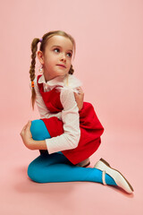 Beautiful, cute, lovely kid. Girl, child in red dress and blue tights posing over pink studio background. Concept of childhood, emotions, fun, fashion, lifestyle, facial expression