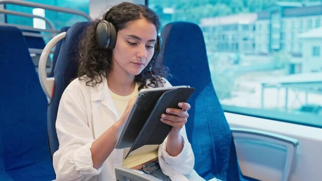 Girl traveler in headphones using tablet computer in train