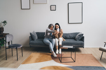 Cheerful mother and daughter taking selfie on smartphone in living room