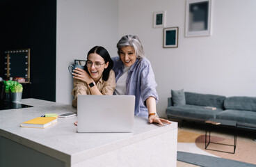 Cheerful mother and daughter laughing while watching funny video on computer