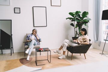 Mother and daughter spending time in living room with laptop and book