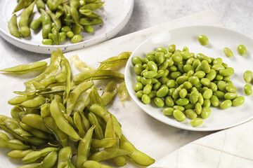 Peeling fresh steamed green soy beans edamame. Japanese plant snack on marble board on light grey background