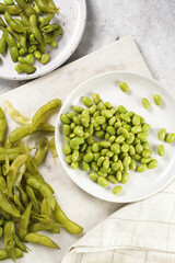 Peeling fresh steamed green soy beans edamame. Japanese plant snack on marble board on light grey background