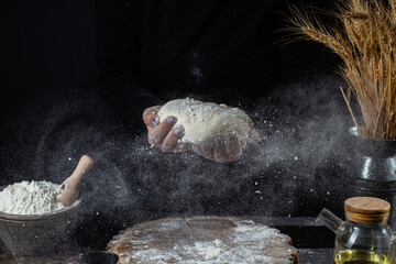 A woman prepares the dough on a dark table. Flour, yeast dough, dark background