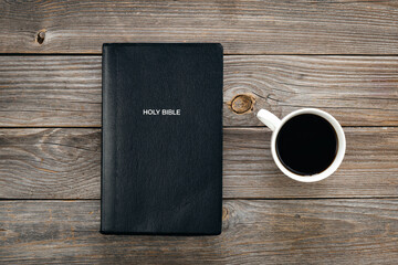 Black Bible and a cup of coffee on a wooden background, top view, concept of christian life, Bible study.