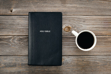 Black Bible and a cup of coffee on a wooden background, top view, concept of christian life, Bible...