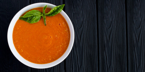 Tomato soup in the white  bowl on the black wooden background. Top view. Copy space.