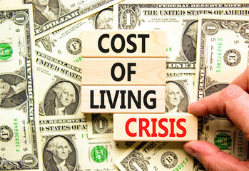 Cost of living crisis symbol. Concept words Cost of living crisis on wooden blocks. Beautiful background from dollar bills. Businessman hand. Business cost of living crisis concept. Copy space.