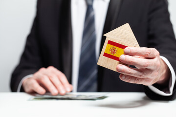 Businessman hand holding wooden home model with Spanish flag. insurance and property concepts