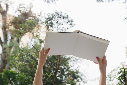 Magazine or book image mockup. Female hands hold an open book against the background of treetops and the sky.