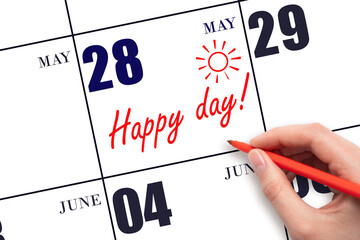 Hand writing the text HAPPY DAY and drawing the sun on the calendar date May 28