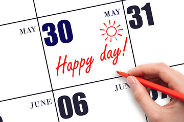 Hand writing the text HAPPY DAY and drawing the sun on the calendar date May 30
