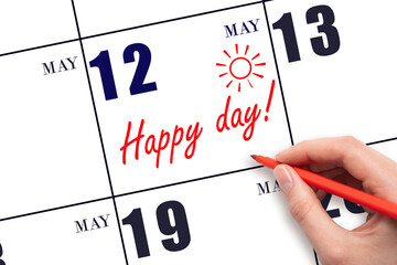 Hand writing the text HAPPY DAY and drawing the sun on the calendar date May 12