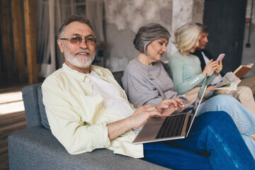 Happy senior man using laptop while sitting on couch with friends