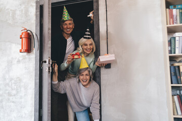 Cheerful aged friends standing at doorstep with presents making surprise