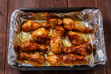 Baked chicken in sauce and herbs on foil on a baking sheet.