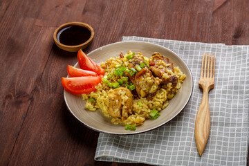 Thai chicken rice garnished with green onions on a wooden table next to a soy sauce napkin and a wooden fork.