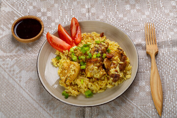 Chicken rice in teriyaki sauce garnished with green onions on a wooden table next to soy sauce on a gray tablecloth next to a wooden fork.