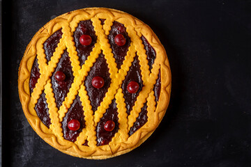Cherry shortcrust pastry pie decorated with cherries and pastry grill on a baking sheet.