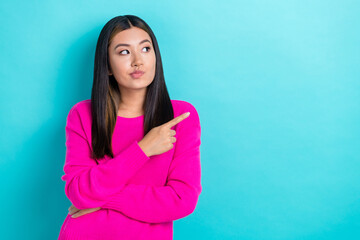 Photo of minded japanese pretty woman wear pink knitted pullover indicate finger empty space pouted lips minded isolated on blue color background