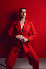 portrait of an elegant sexy woman in a red jacket and pants stands against the background in the studio. Femininity, feminism and fashion.