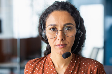 Serious and concentrated woman with video call headset looking at camera, hispanic woman thinking...
