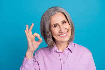 Photo of positive adorable lady pensioner trendy clothes arm okey symbol nice feedback beauty procedure isolated on blue color background