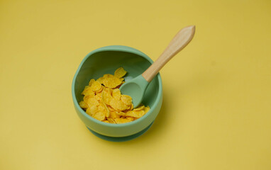 Children's silicone bowl with corn flakes. Baby feeding and nutrition concept. Top view, flat lay.