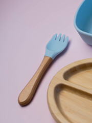 A set of colored children's silicone forks and spoons next to a wooden plate. Baby feeding and nutrition concept.