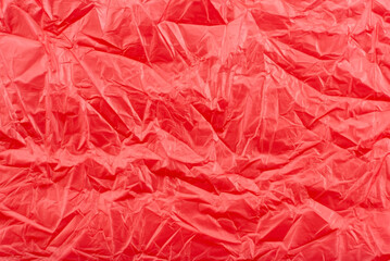 Texture of crumpled transparent polyethylene on a pink, red background, full frame