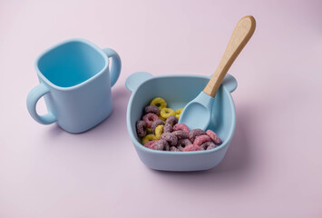 A set of children's silicone dishes with corn flakes. Baby feeding and nutrition concept. Top view, flat lay.
