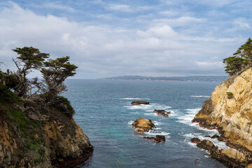 Fototapeta na wymiar Ocean view at Point Lobos State Natural Reserve, Carmel, California, USA, featuring the old cypress grove and rocks against a partly cloudy sky and plenty of space for copy