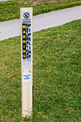 Marker for natural gas pipeline - cathodic test station stuck into green grass by sidewalk - Warning in English and Spanish - obrazy, fototapety, plakaty