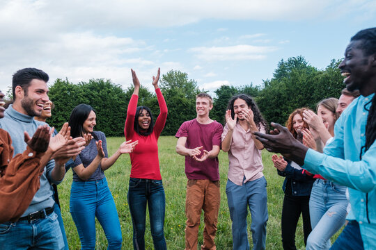 Heterogeneous group of young people from diverse backgrounds clapping together outdoors. Concept: Integration, lifestyle, friendship