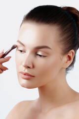 Fototapeta premium Young woman applies eye shadow with brush. Skin care, cosmetics and beauty. Closeup, natural makeup