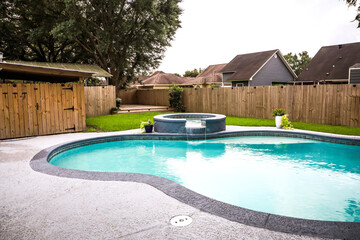Free-form gray grey accent swimming pool with turquoise blue water in a fenced-in backyard in a suburban neighborhood