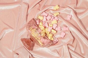 Romantic creative layout with crystal bowl and spilled gummy bears on pastel pink velvet background. 80s or 90s retro fashion aesthetic love concept. Minimal romantic idea.