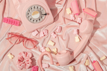 Valentines day creative layout with hair rollers, eyeglasses, scrunchie, spilled gummy bears and rotary phone handset on pastel pink velvet background. 80s or 90s retro fashion aesthetic love concept.