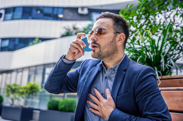 Stress and asthma. Young businessman treating asthma attack with inhaler. Health care concept