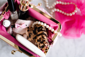 Fototapeta na wymiar Pink cosmetic bag fill with make up products and jewelry on marble table top view closeup. Beauty concept.