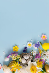 Stylish Easter eggs in nest, colorful flowers and cherry blossoms flat lay on blue background with...