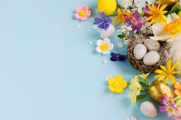 Happy Easter! Easter eggs in nest, colorful flowers and blooming cherry petals flat lay on blue background. Stylish festive template with space for text. Greeting card or banner
