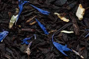 Closeup of black tea with orange, lemon peels and cornflower petals background