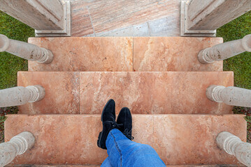 A man in jeans and black shoes on the marble steps. Men's feet on the steps. View from above.