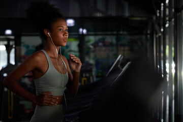young sports woman working out with wired earbuds and running on treadmill in gym