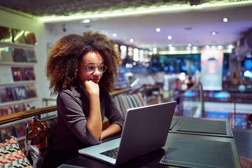 young afro black brazilian woman sitting in a library cafeteria reading the screen of her notebook