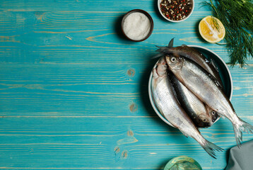 Small raw fish in a bowl, pike perch. On a blue wooden background, with lemon, herbs, salt. Top view